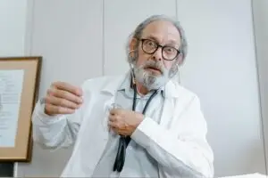 Elderly male doctor with glasses using stethoscope indoors during a medical consultation.